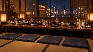 深夜の居酒屋の座敷で、長いテーブルの手前に誰も座っていない座布団が4つ並んでいるイラスト